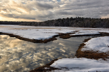 Winter landscape. River with reflective clouds at sunset and coniferous forest. coast of the Atlantic Ocean. USA. Maine.