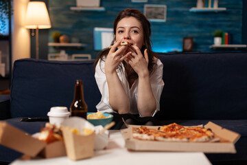 Portrait of woman watching comedy movie eating tasty delivery pizza slice relaxing on sofa in...