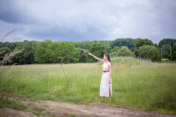 A Hungarian woman standing on the field in a linen dress with a whip