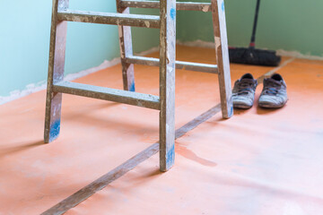 Foot of a ladder in the middle of a room. Floor covered by household works.