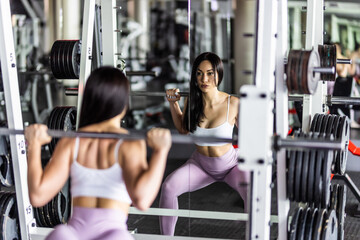 Fototapeta premium Fit woman doing squat with barbell in the gym hall