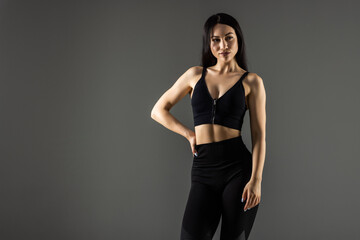 Tough young woman standing on grey background. Muscular female looking at camera.