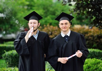 oung male graduate student in a black robe and a square hat smokes his diploma or certificate. Marijuana, cannabis and student life.
