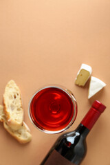 Bottle and glass of wine, cheese and bread on beige background