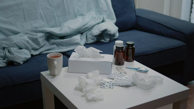 Close up of empty living room with medical treatment on table. Nobody in space with medicaments, medicine, bottles of pills, capsules, thermometer and tissues for patient with disease