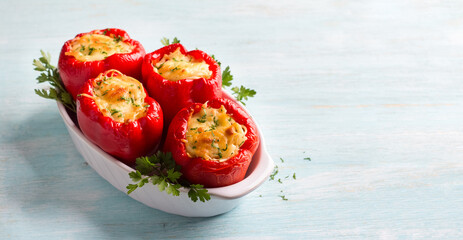 Bell red peppers stuffed with pasta, vegetables, cheese and herbs in baking dish on light blue...