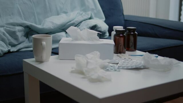 Close up of coffee table with medicine and bottle of pills. Nobody in living room with medicaments, capsules, box of tissues and thermometer. Empty space for sick patient and healing treatment