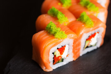 Japanese cuisine. Salmon rolls with avocado. Japanese food on a black background. Green caviar of flying fish. Tobiko. Macro photography of sushi. Close-up of the rolls