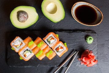 Japanese cuisine. Salmon rolls with avocado. Japanese food on a black background. Sliced avocado. Sushi , tobiko and soy sauce. Place for text in food photos.