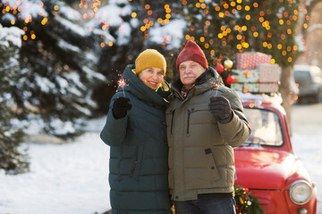 Senior couple pensioners in warm winter clothes with sparkler fireworks in the street. merry Christmas!