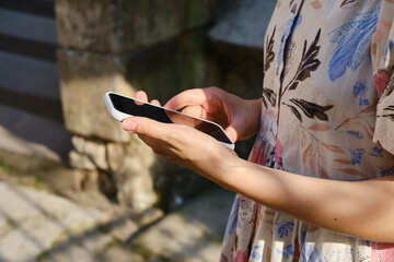 A girl on the street is holding a modern smartphone, sending a text message or using an application on her mobile phone. View city map using smartphone. Smartphone close-up