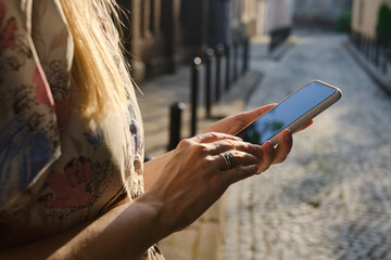 A girl on the street is holding a modern smartphone, sending a text message or using an application on her mobile phone. View city map using smartphone. Smartphone close-up