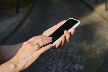 A girl on the street is holding a modern smartphone, sending a text message or using an application on her mobile phone. View city map using smartphone. Smartphone close-up