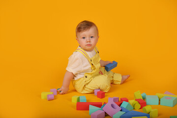 a beautiful blue-eyed little boy in a yellow suit plays with colorful toys