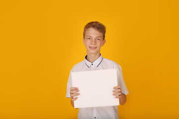 a handsome guy in a white shirt holds a white sheet of paper yellow background