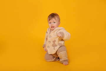 a beautiful blue-eyed baby is sitting on a yellow background in a knitted suit