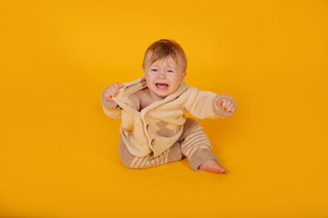 a beautiful blue-eyed baby is sitting on a yellow background in a knitted suit