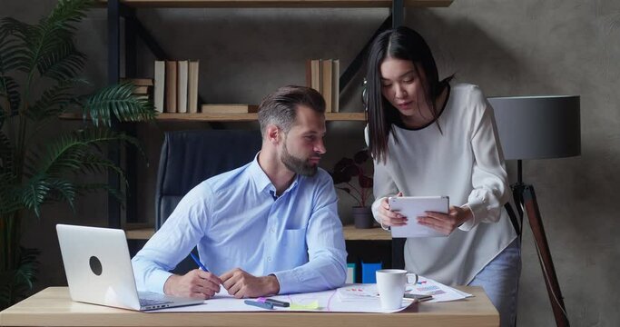 Businessman and Asian assistant female colleagues discuss financial data analyzing marketing result using digital tablet in office and collate report using laptop having business conversation help