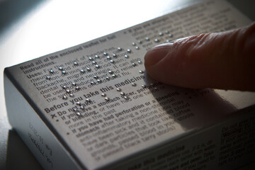 Mans finger reading braille instructions on a medicine packet