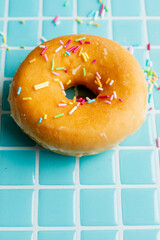 Aerial view of a classic donut with colored noodles, on a light blue background, vertically, with copy space