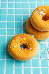 Top view of classic donuts with colored noodles, on light blue background, in vertical, with copy space