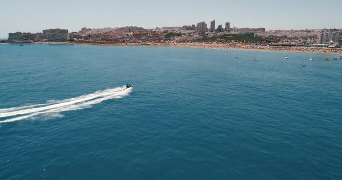 Drone following fast riding watercraft who approaches to the La mata beach of tourist city Torrevieja during summer vacations in Spain. People enjoying of sunny day