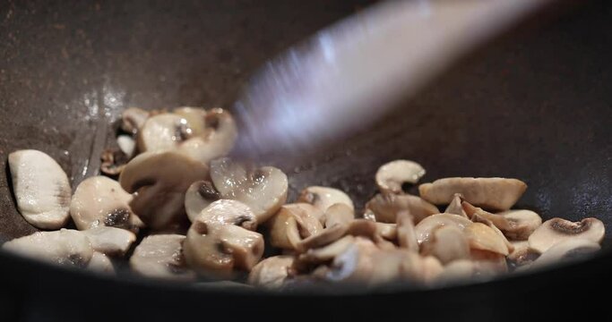 Fried mushrooms in pan are stirred with wooden spatula close-up