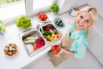 Top angle view of good looking smiling cheerful woman grandmother in apron washing vegetables...