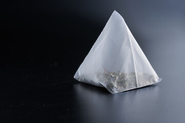 Pyramid tea bag with green tea on a dark polished gradient surface. Macro. Free space for an inscription.