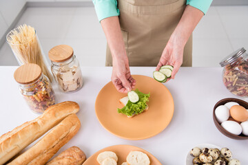 Top angle cropped photo of grandmother prepare homemade meal breakfast put salad lettuce sliced cucumber on bread at home