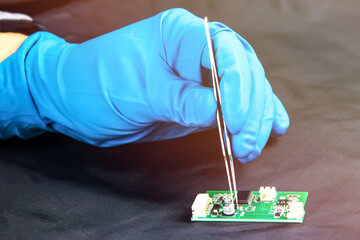 Hand in blue glove holds tweezers on pcb