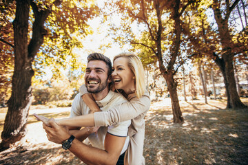 Boyfriend carrying his girlfriend on piggyback in autumn park.