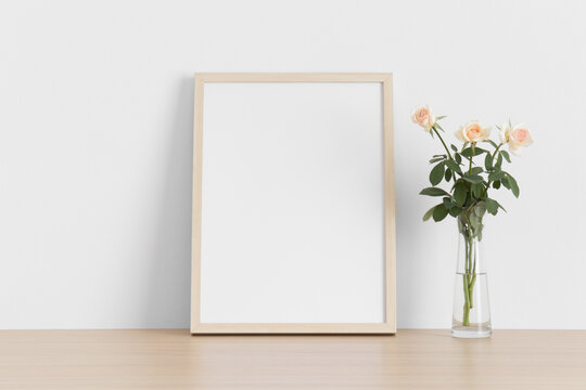 Wooden frame mockup with a bouquet of a pink roses on the wooden table.