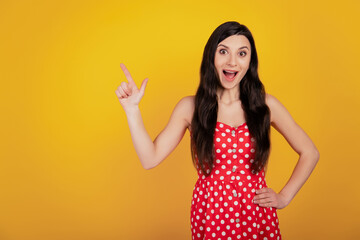 Portrait of shocked funny woman finger indicate up empty space open mouth wear dotted red dress on yellow background