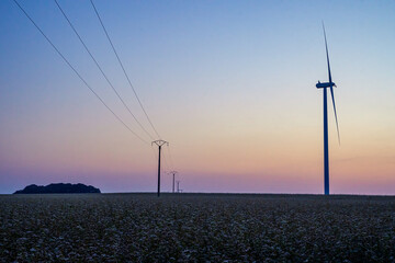 Fototapeta na wymiar Night falling on the Countryside over a Field with Power Line and Wind Turbine
