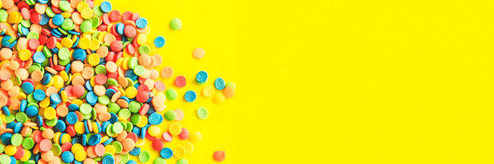 Fototapeta na wymiar Colorful round candies are neatly scattered on a yellow background. The banner. Flat lay, top view