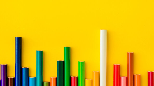 Colored pencils are arranged in a row on a light yellow background. One white pencil sticks out above all. Gradient color. Concept: development jumps, stock exchange jumps.
