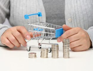 the woman sits at the table and holds a miniature cart and stacks of white coins. Concept of savings