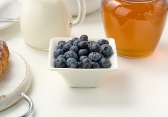 ripe blueberries in a white ceramic plate on a white table, breakfast ingredients