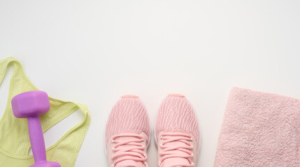 a pair of pink sneakers, a terry towel and a plastic dumbbell on a white background, top view