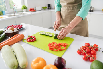 Cropped photo of housewife lady arms hold knife cut cucumber make salad wear apron kitchen room indoors