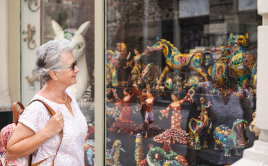 Traveler senior woman visiting Barcelona, looking artistic creations in a shop window. Happy retired enjoying vacations