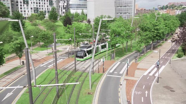 View of the Bilbao tram as it passes through gardens while a bicycle passes along the bike path. Green and sustainable city. 