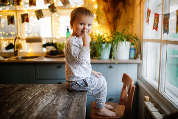 Caucasian Child Toddler sits on the table and picks his nose, festive mood and bad habits. The concept of birthday and Christmas, preparation of the holiday and children's emotions