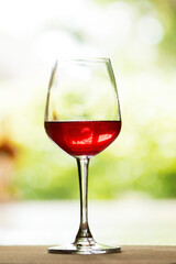 A glass of red wine is placed on a natural background wooden floor.