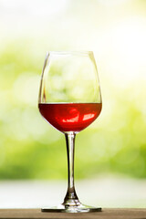 A glass of red wine is placed on a natural background wooden floor.