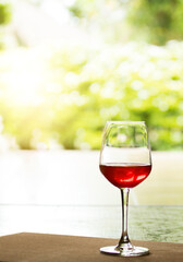 A glass of red wine is placed on a natural background wooden floor.