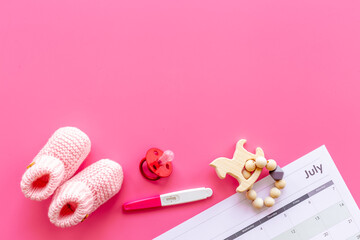 Pink baby girl booties with pregnancy test on calendar, top view