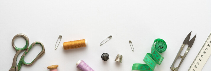 Flat lay composition with threads, scissors, buttons, needles, pins and other sewing accessories on white background. Long banner, top view, copy space, flat lay, mock up. Spase for text