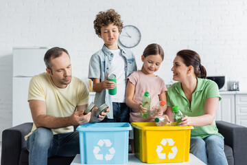 Smiling family sorting trash together in boxes with recycle symbol - obrazy, fototapety, plakaty
